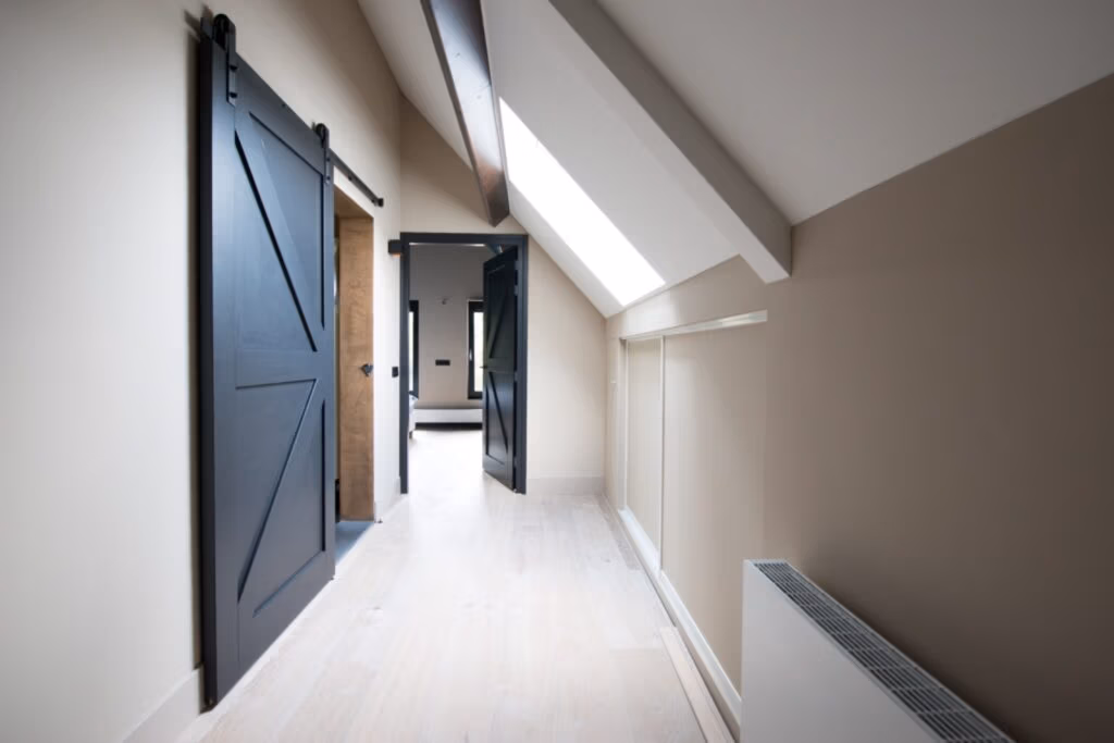 Lichte hal met een schuin plafond, zwarte deuren en een houten vloer, leidend naar een naastgelegen kamer.