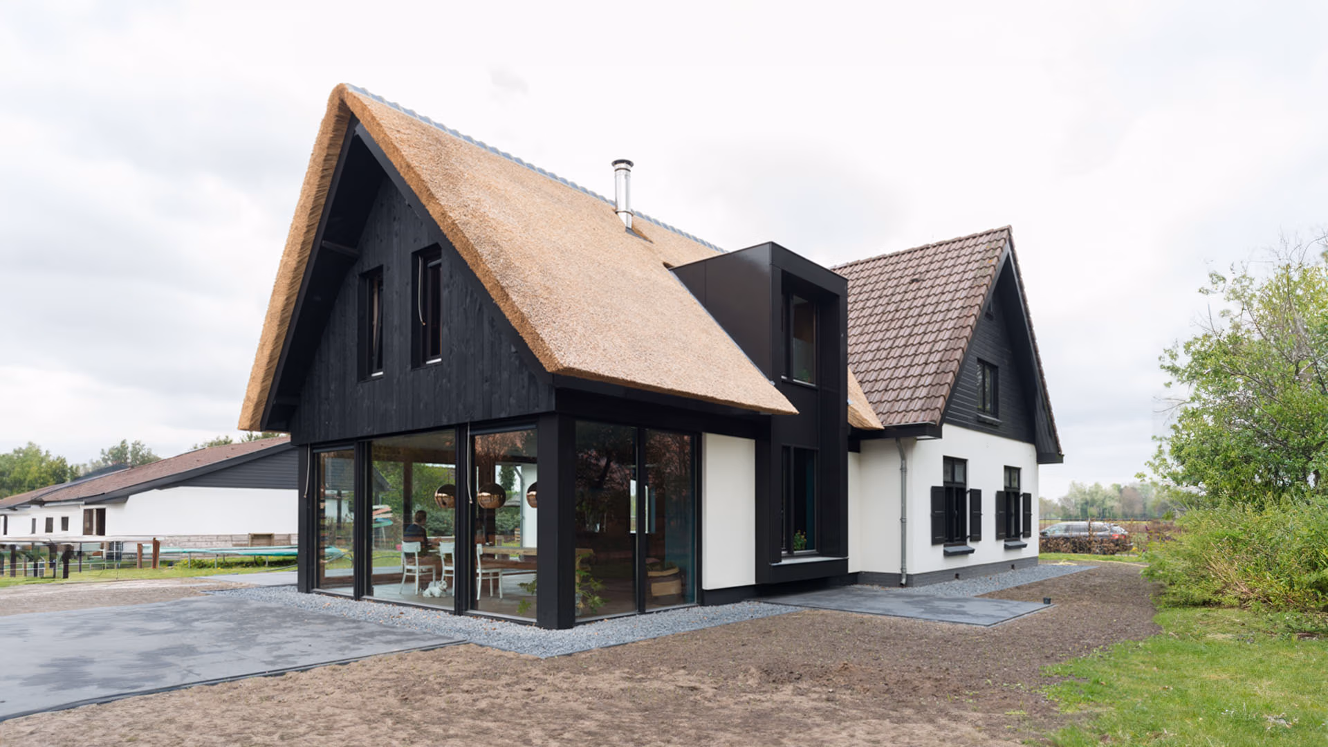 Een modern landhuis met een rieten dak en zwarte houten gevelaccenten, gecombineerd met grote glazen ramen en witte muren.