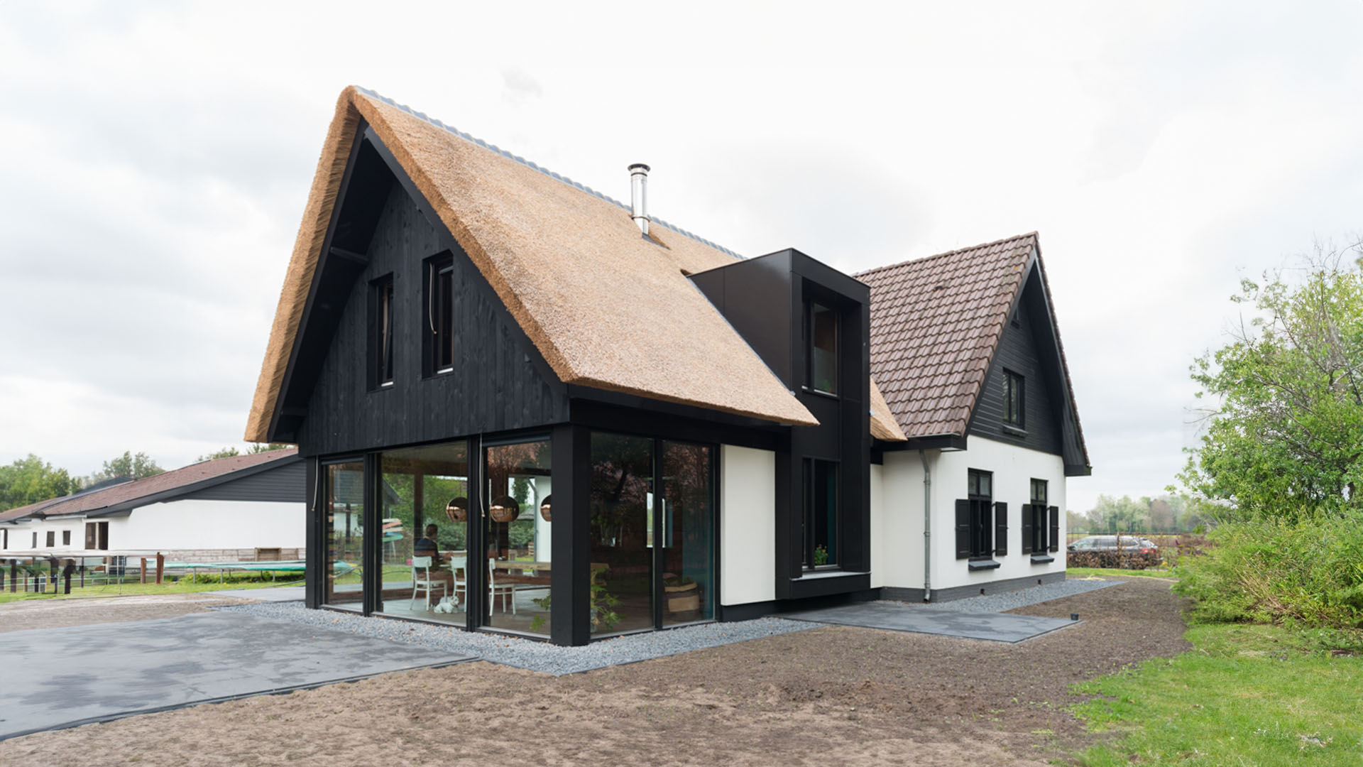Een landelijk huis met een rieten dak en zwarte elementen, met grote ramen die natuurlijk licht binnenlaten.