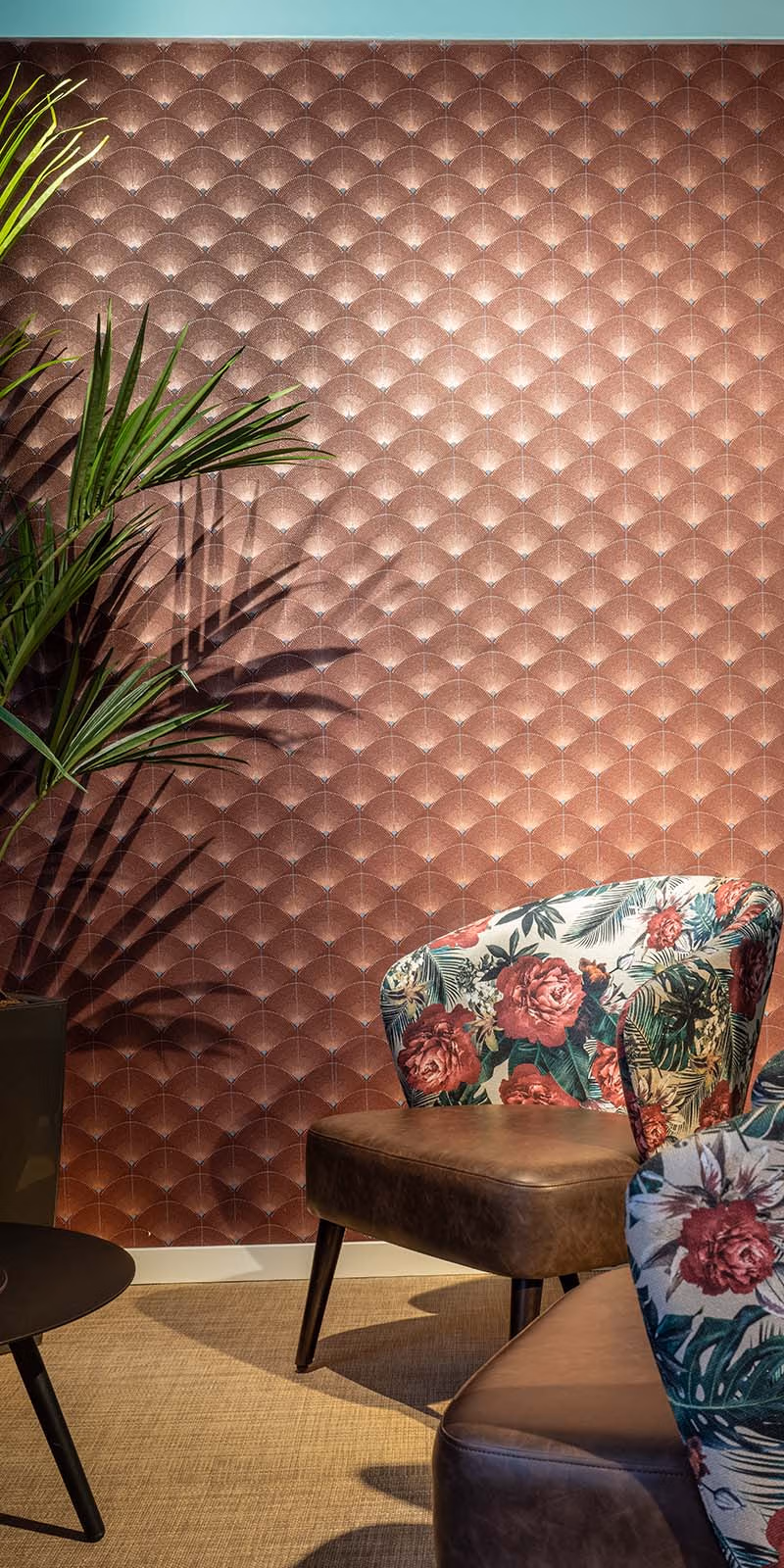 Wand bekleed met luxe koperen wandpanelen in een 3D-patroon, omgeven door een groene plant en een stoel met een bloemenprint, gelegen in een sfeervolle ruimte.