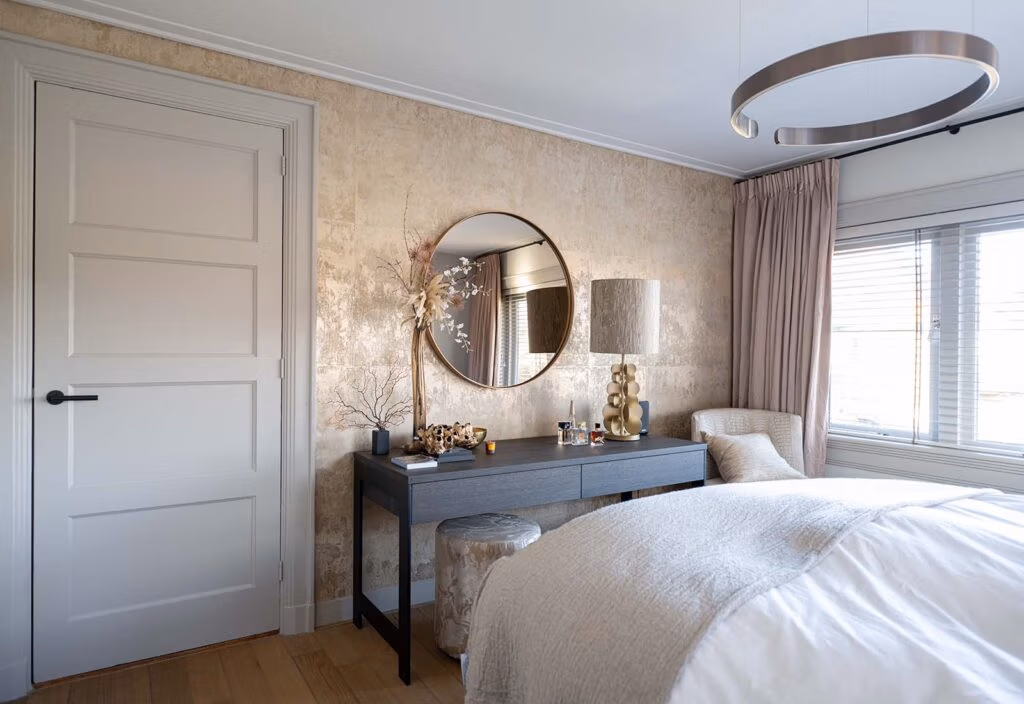 Slaapkamer met een elegante uitstraling, voorzien van een gouden metallic wand, een ronde spiegel met decoratie, een donkergrijze console en zachte pastelgordijnen.